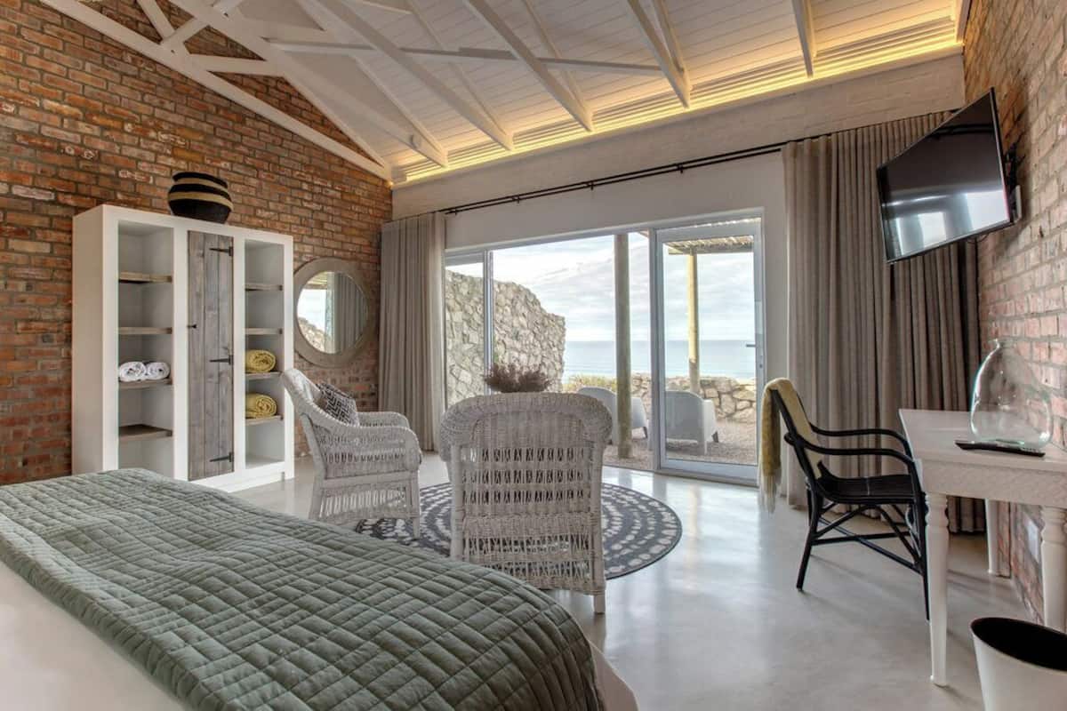 A modern bedroom with a large bed, a white wardrobe, wicker chairs, a round table, and a TV.