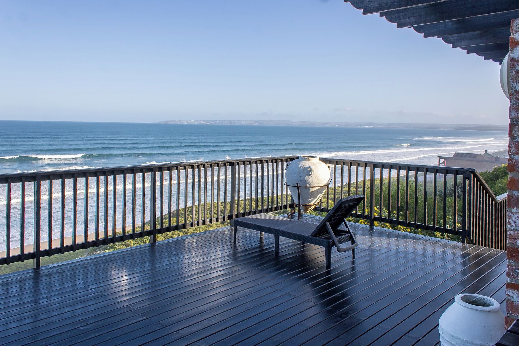 A wooden deck with a view of the ocean, a white pot, and a chair.