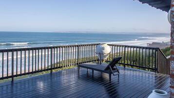 A wooden deck with a view of the ocean, a white pot, and a chair.