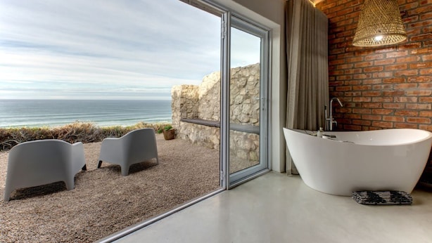 Un baño moderno con una bañera grande, una pared de piedra y vista al océano.