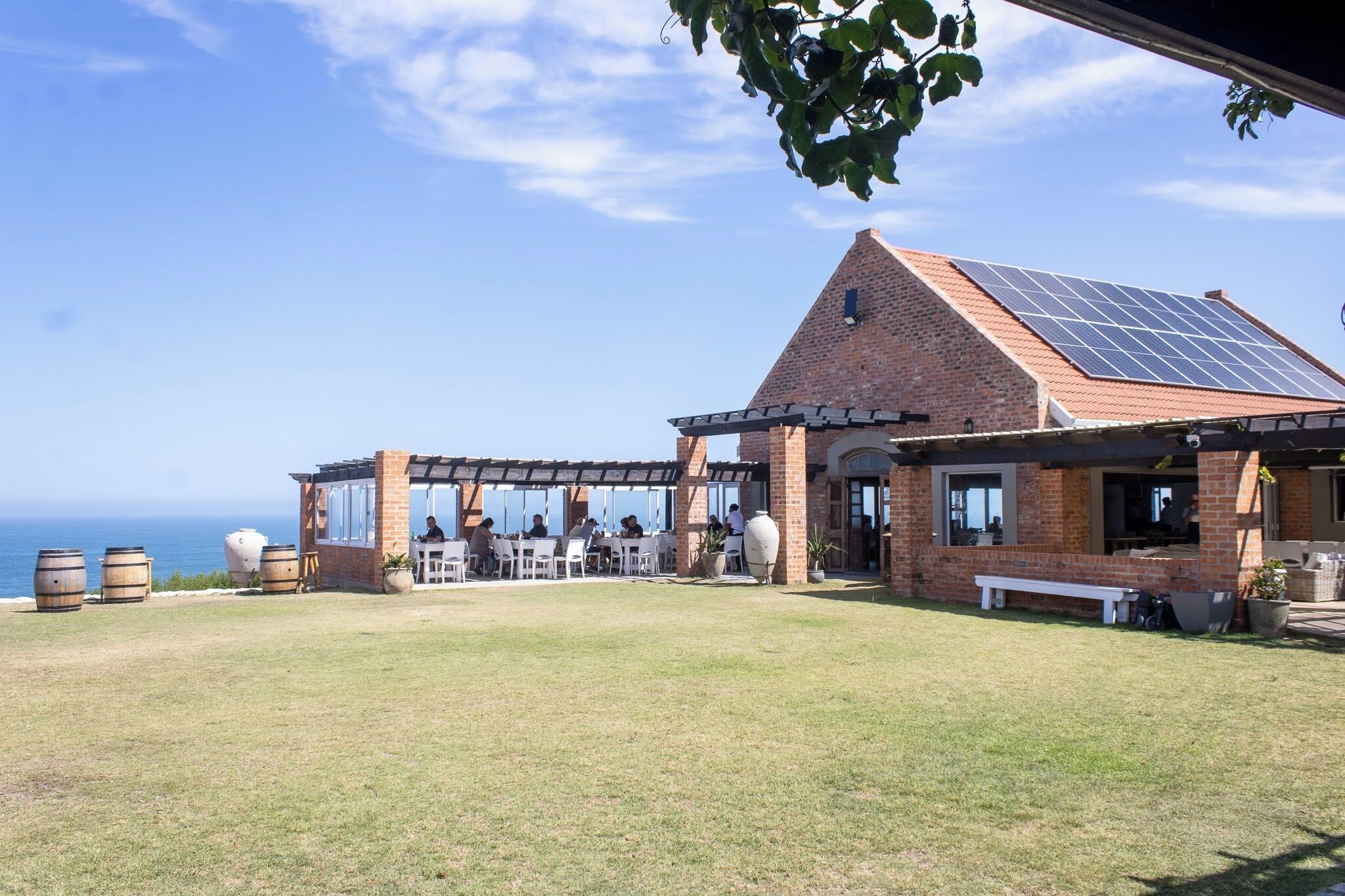 A building with a brick exterior, a sloped roof with solar panels, and an outdoor seating area with tables and chairs.