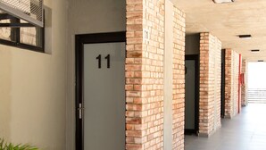 A corridor with a brick wall, a door labeled '11', and a potted plant. - Wild Olive 11 (Windhoek)