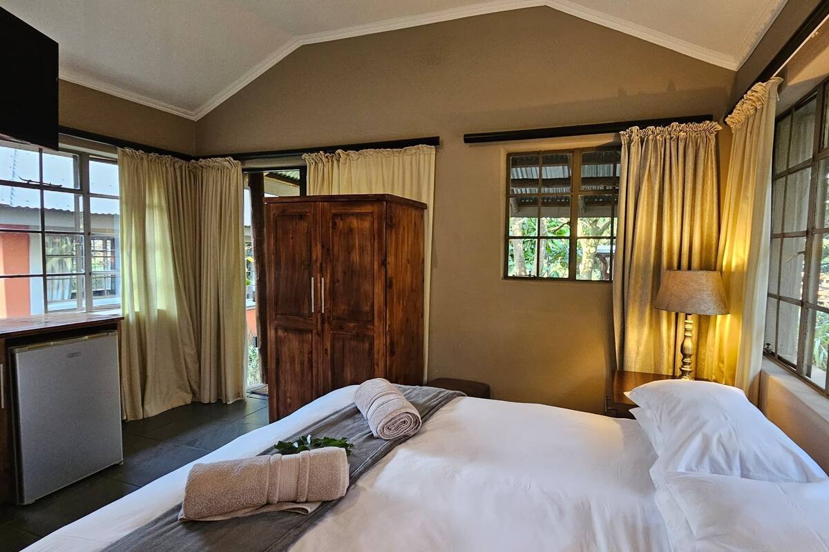 A hotel room with a bed, a desk, a wardrobe, and large windows with curtains.