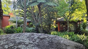A large rock in the foreground, a small wooden structure with a roof, and lush greenery in the background. - Lidwala Lodge  (Ezulwini)
