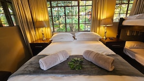 Habitación de hotel con una cama grande, dos mesitas de noche con lámparas, una ventana con cortinas y vistas a zonas verdes.