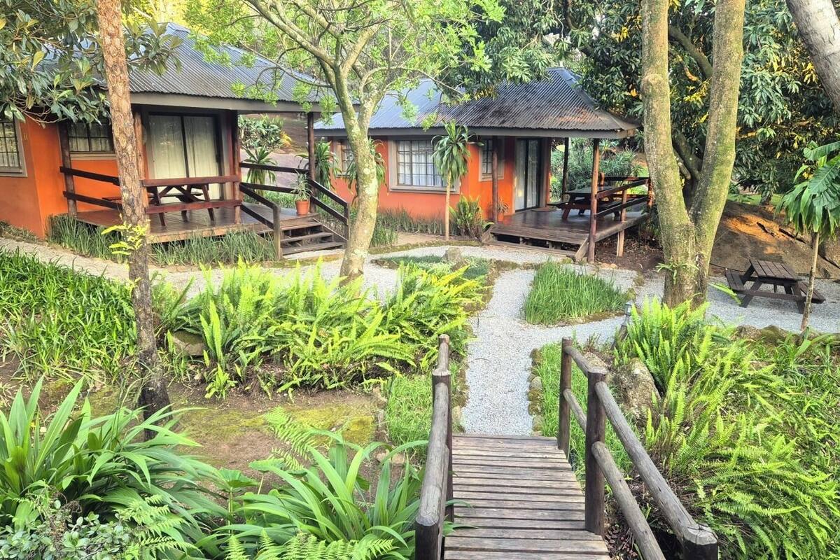 A wooden bridge leading to a bungalow with a porch and a small garden area.