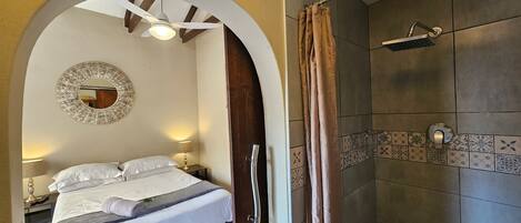 A bedroom with a bed, a mirror, and a shower area with tiled walls.