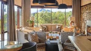 A modern dining area with a long wooden table, multiple chairs, and hanging black pendant lights. - Ecca Lodge (Makhanda)
