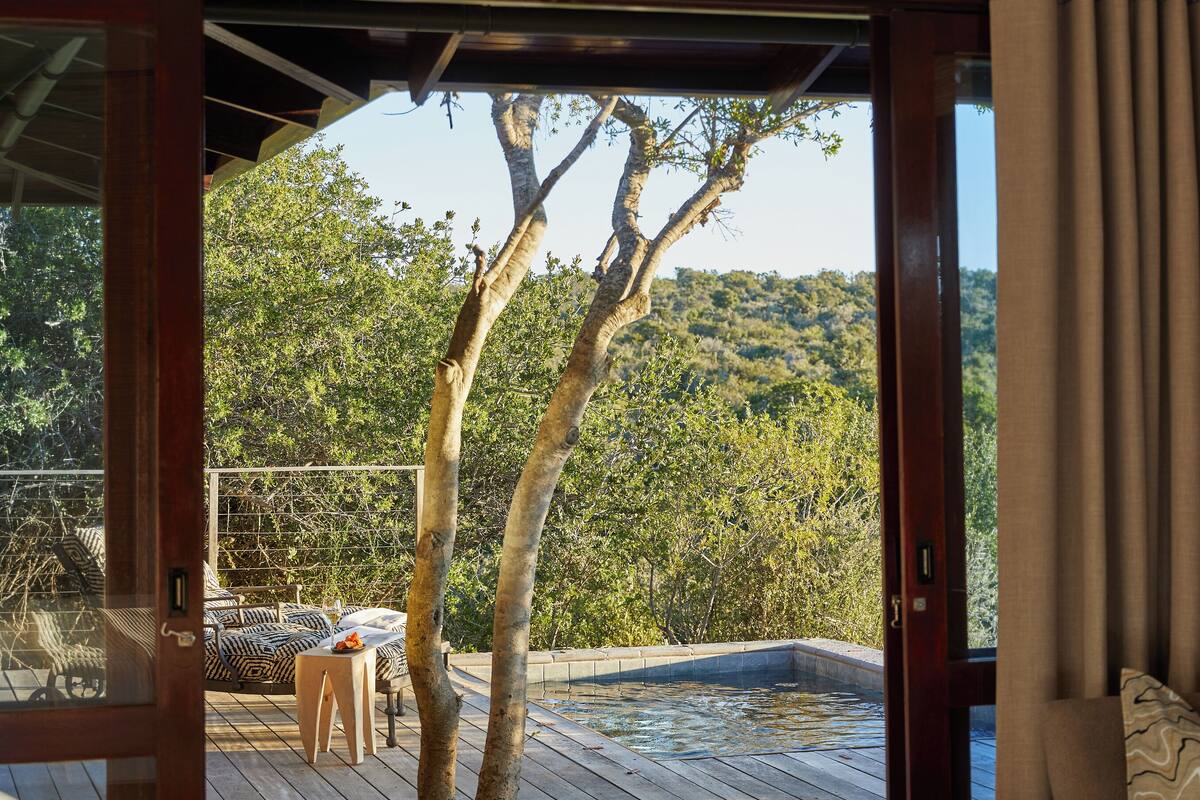 Un dormitorio con una puerta de madera grande que da a una terraza exterior con un jacuzzi y vistas a una ladera boscosa.