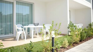 Un espace extérieur moderne aménagé avec des chaises en plastique blanc et une table, entouré d’un jardin bien entretenu avec différentes plantes et un petit lampadaire.