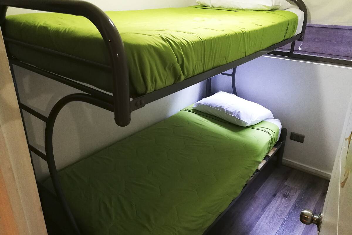 En køjeseng med grønt sengetøj og en hvid pude.