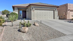 A single-story house with a garage, surrounded by a gravel driveway and desert landscaping including cacti and small trees.