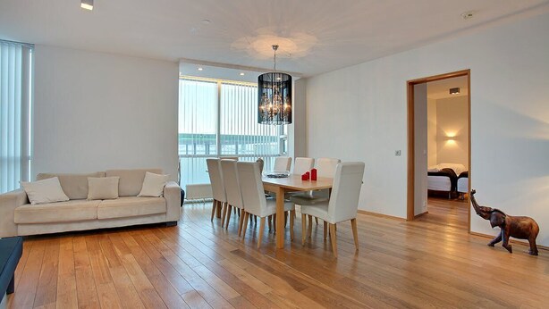 Un salon moderne avec un plancher en bois, un canapé beige, une table à manger avec des chaises et un lustre.