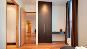 Une chambre d’hôtel avec un plancher en bois, une armoire sombre, une petite table avec une plante et deux lits.