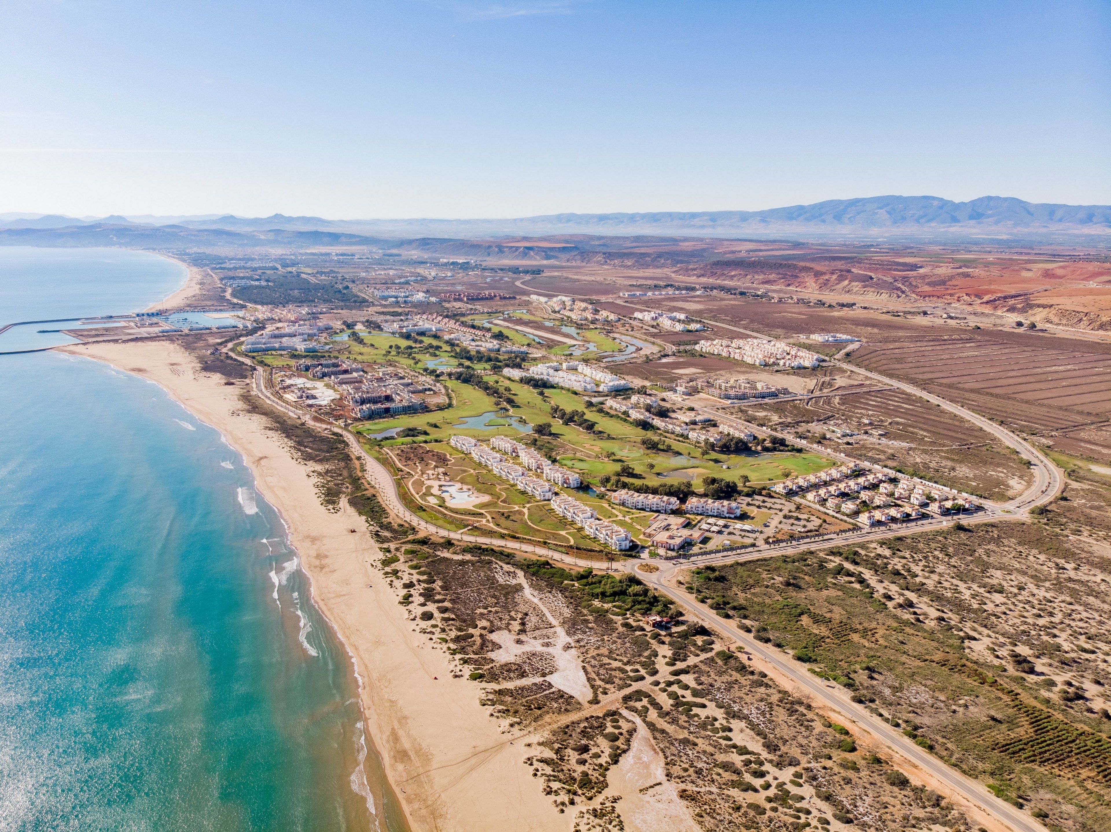 An aerial view of a coastal resort with multiple buildings, a beach, and a golf course.
