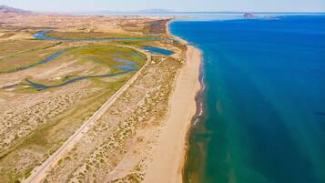 An aerial view of a coastal area with a sandy beach, a winding river, and a clear blue sea.