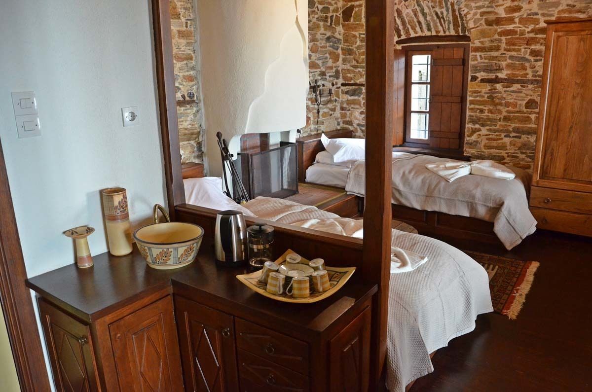 A rustic bedroom with a stone wall, wooden furniture, and a bed with white linens.