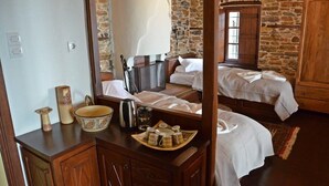 A rustic bedroom with a stone wall, wooden furniture, and a bed with white linens. - Fyloma (South Pelion)
