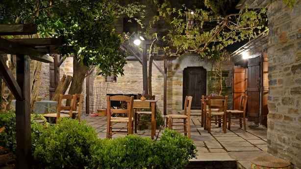 An outdoor seating area with wooden tables and chairs, surrounded by stone walls and greenery. - Fyloma (South Pelion)