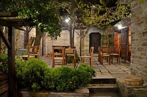 An outdoor seating area with wooden tables and chairs, surrounded by stone walls and greenery. - Fyloma (South Pelion)