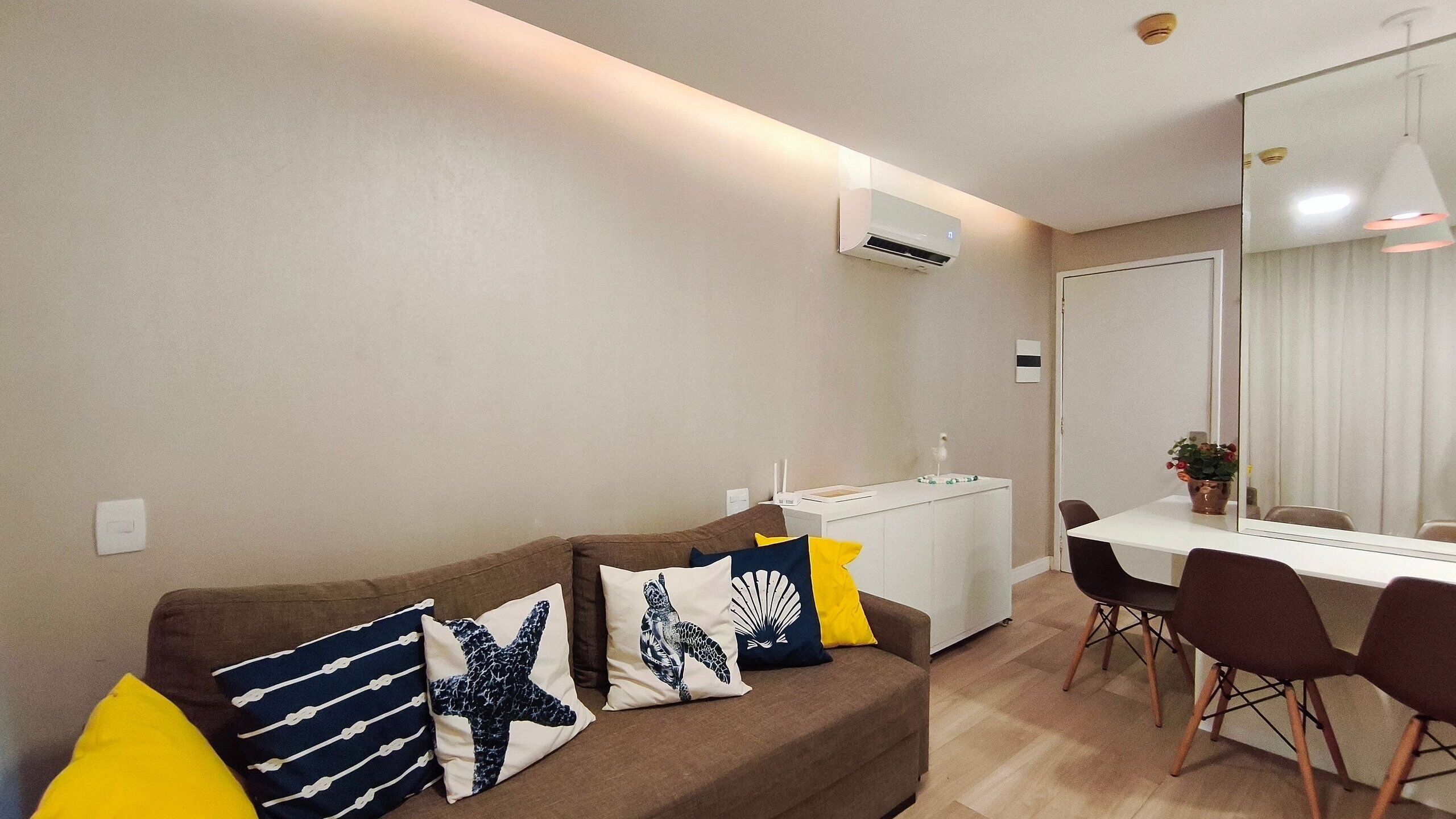Una sala de estar con un sofá marrón, una mesa blanca y una zona de comedor con sillas.