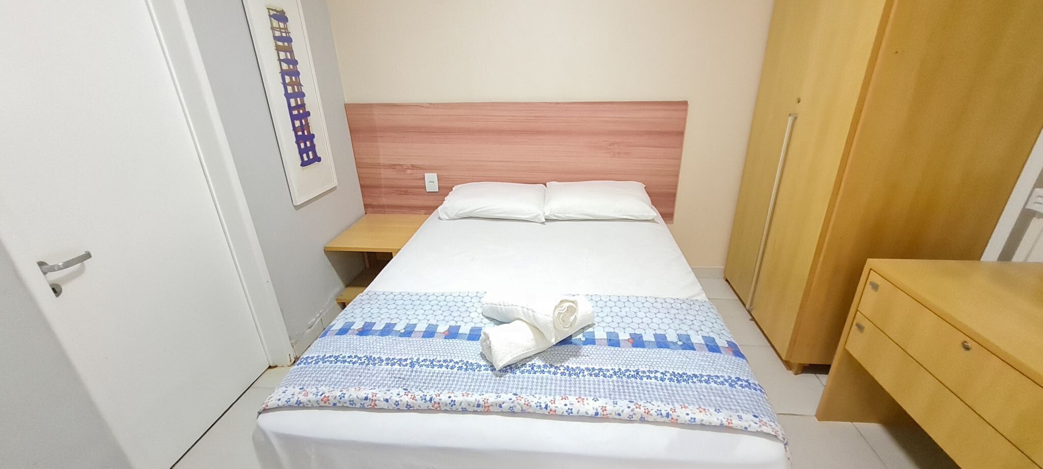 Ett hotellrum med en säng, ett träbord vid sängen, en garderob och en dörr.