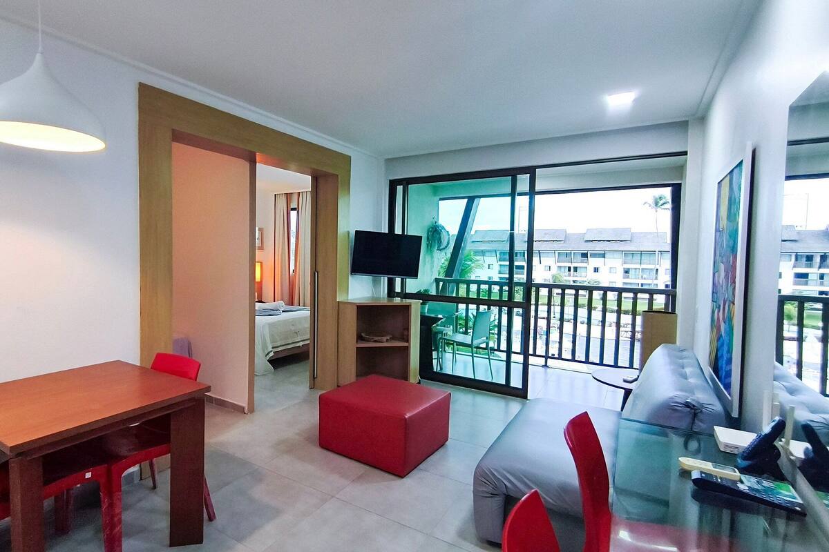 A modern living room with a dining area, a TV, and a balcony with a view.