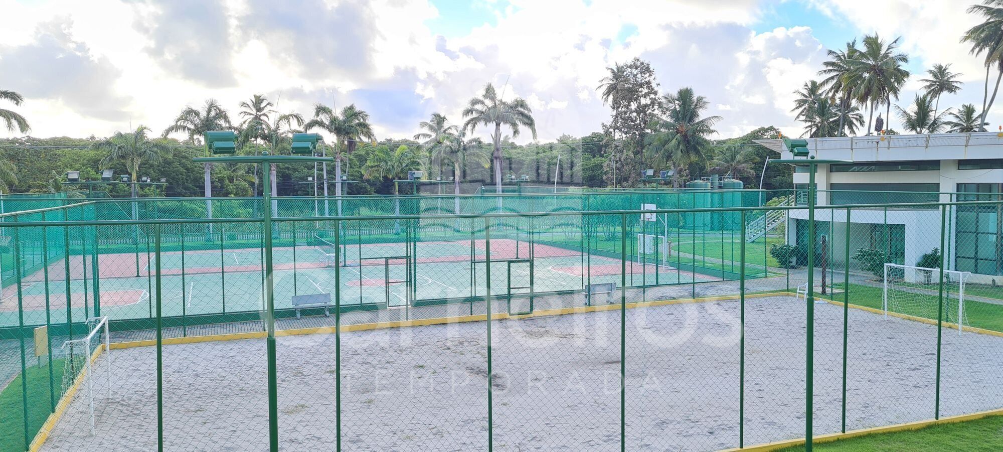 Un campo sportivo con recinzione verde, una panchina e un edificio sullo sfondo.