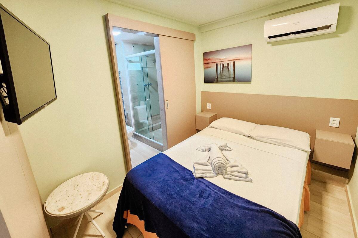 A hotel room with a bed, a small round table, a shower area, and a wall-mounted air conditioner.