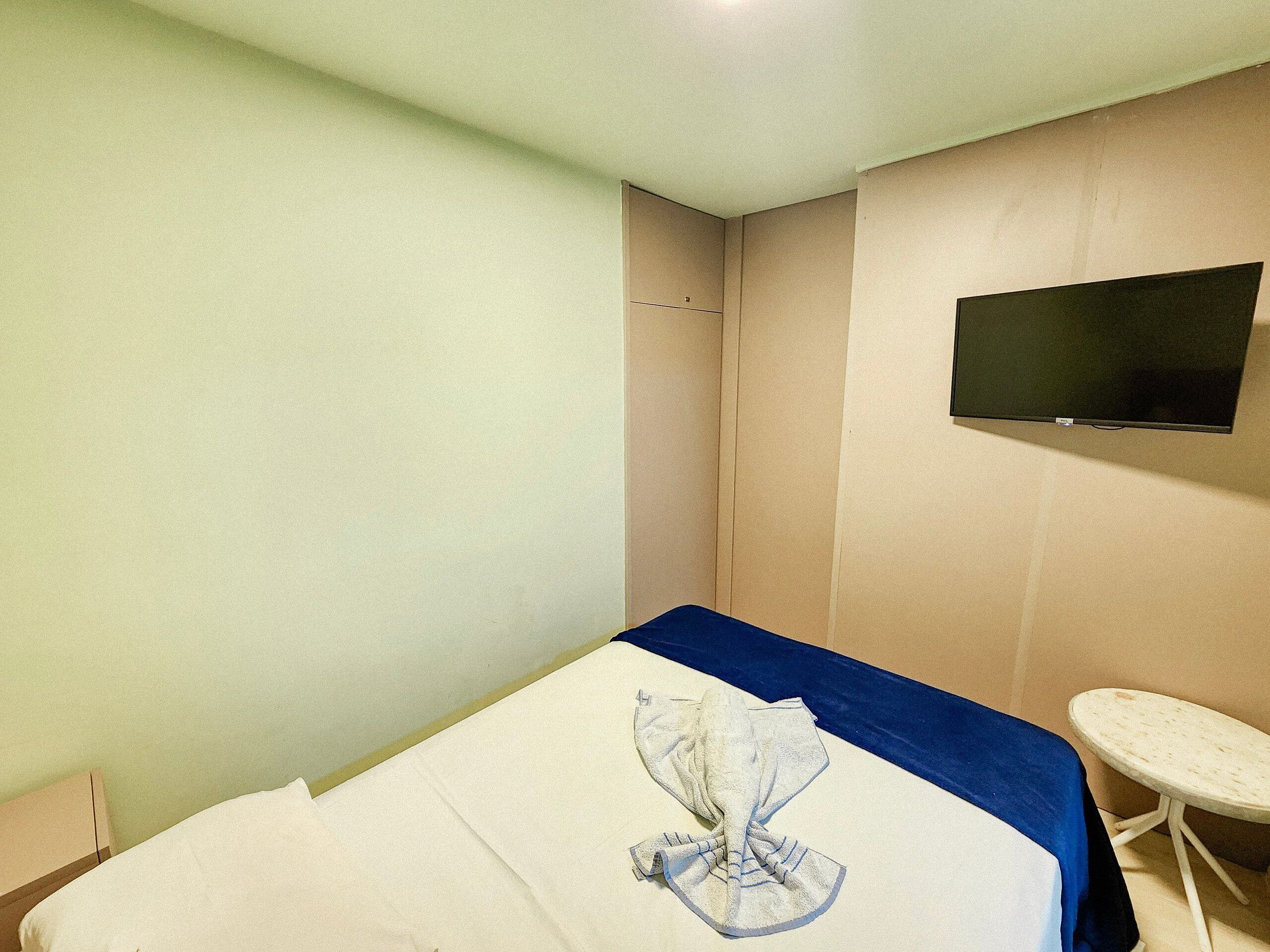 Ein Hotelzimmer mit einem Bett, einem flachbildfernseher an der Wand und einem kleinen Tisch.
