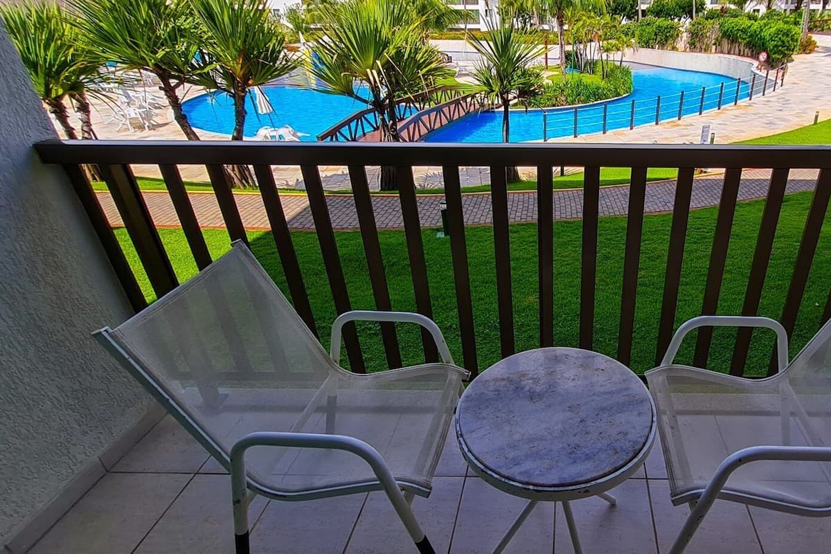A balcony with two chairs and a small table, overlooking a pool and green lawn.