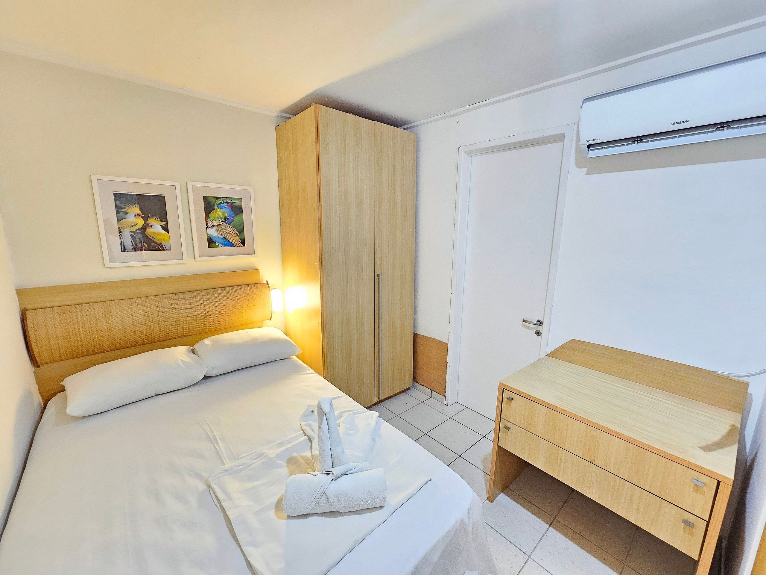 A hotel room with a bed, a wardrobe, a desk, and an air conditioning unit.