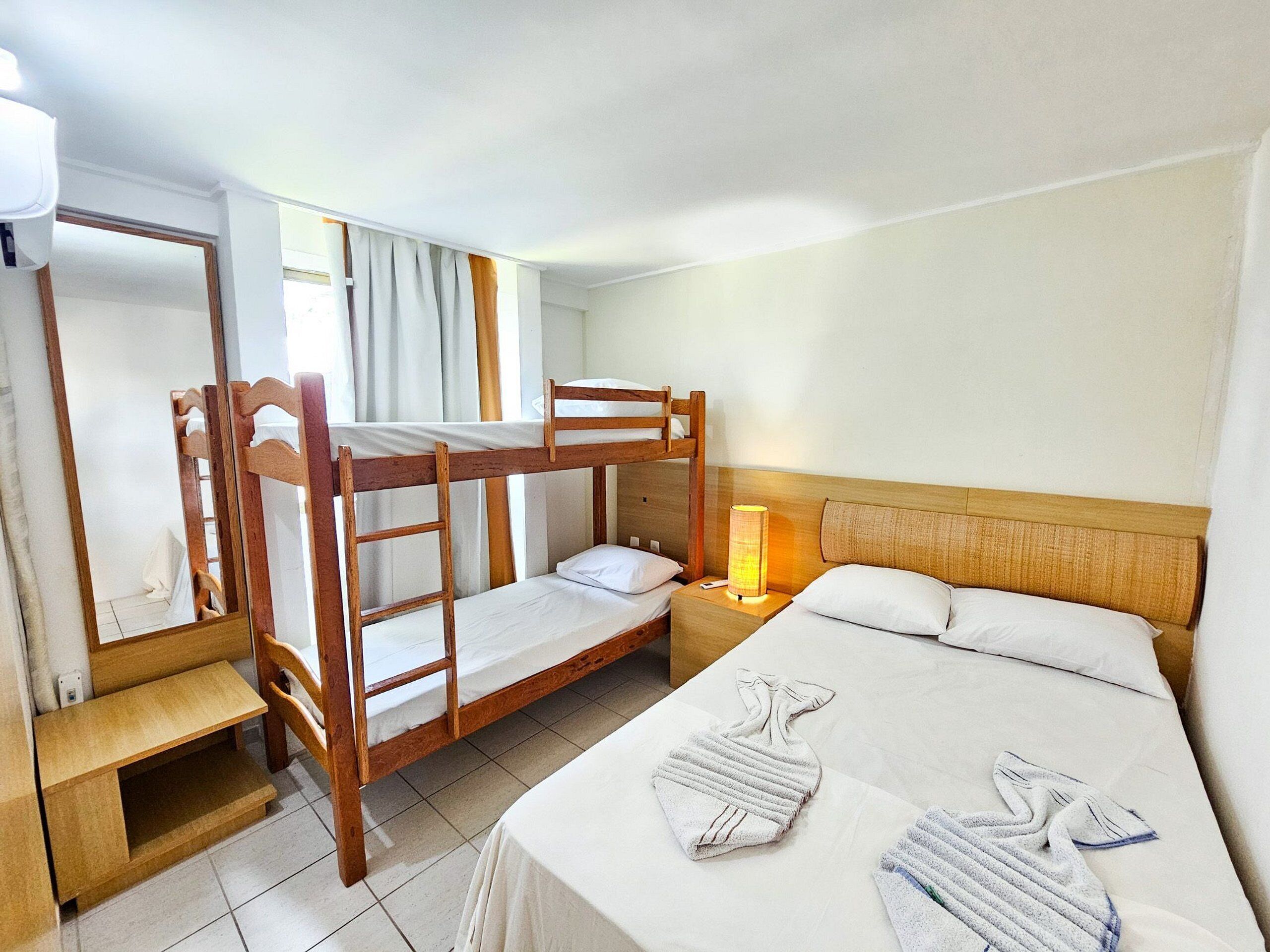 A bunk bed room with a wooden headboard, a bedside table with a lamp, and a bathroom mirror.