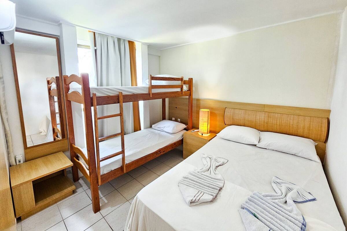 Une chambre avec un lit superposé doté d’une tête de lit en bois, une table de chevet avec une lampe et un miroir dans la salle de bain.