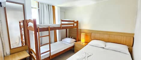 A bunk bed room with a wooden headboard, a bedside table with a lamp, and a bathroom mirror.
