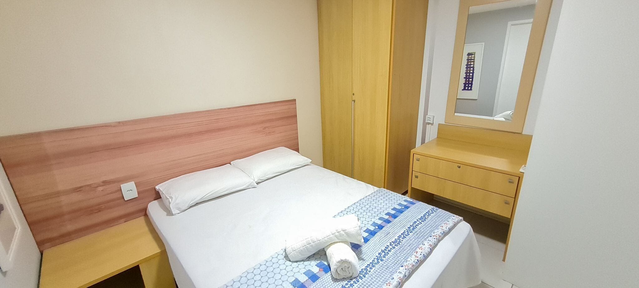 A hotel room with a bed, a wooden headboard, a bedside table, a mirror, and a wardrobe.