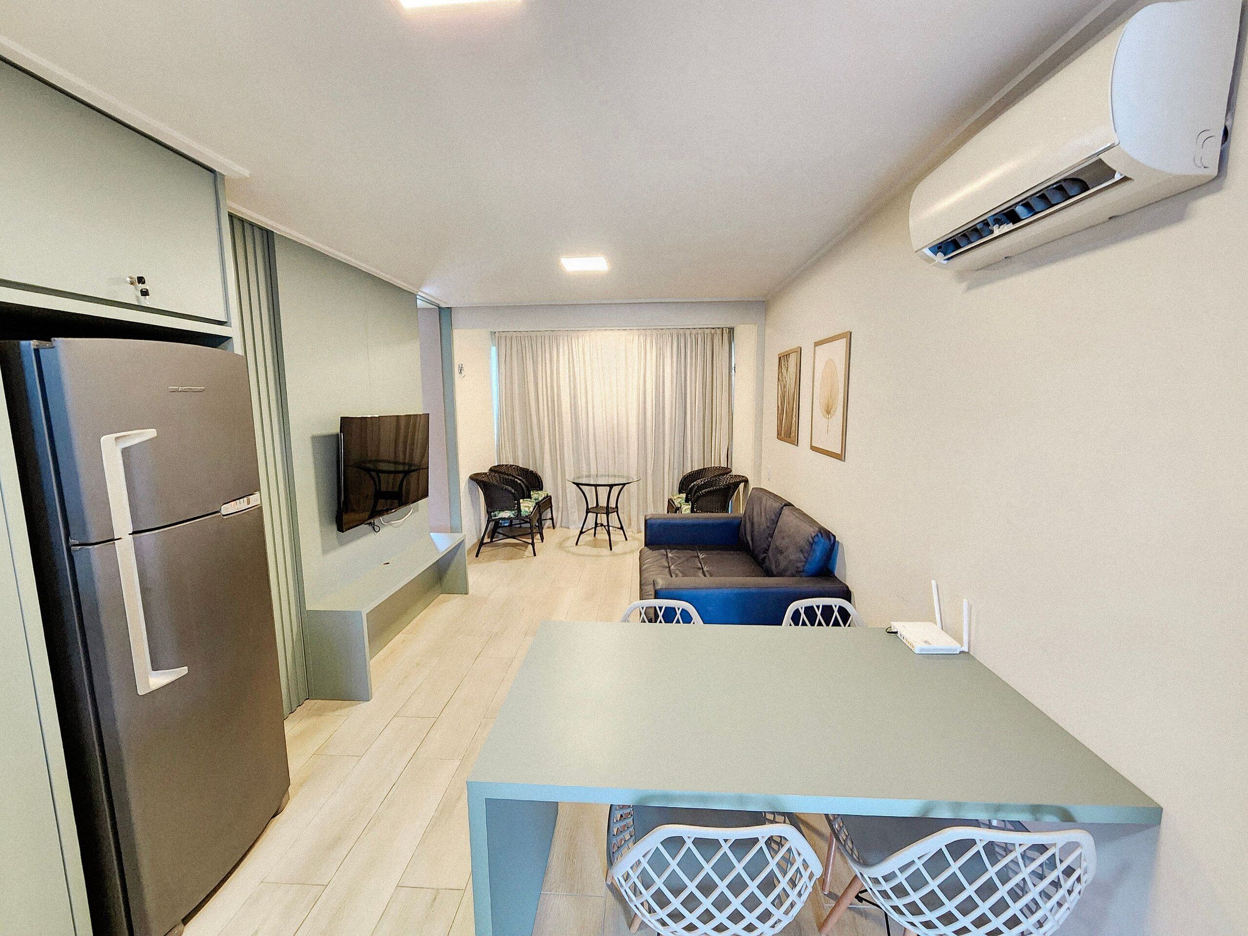 A compact living space with a kitchenette, a flat-screen TV, a sofa, a dining table, and a chair.