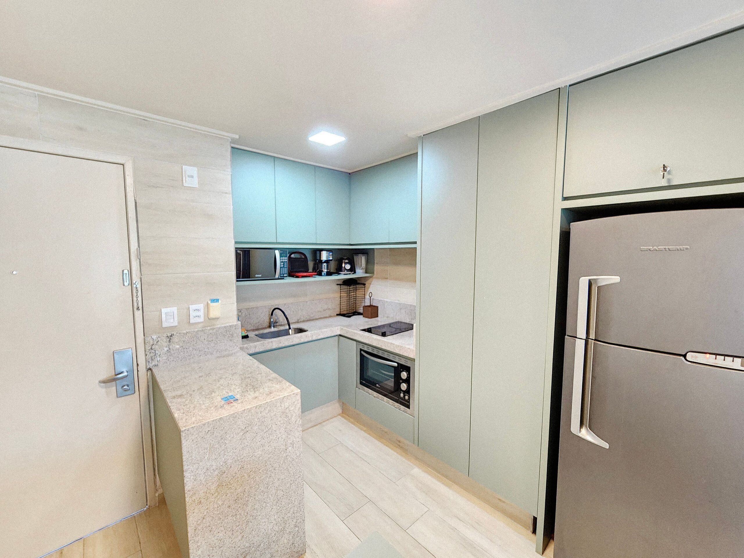 A compact kitchen with a built-in oven, a microwave, and a stainless steel refrigerator.