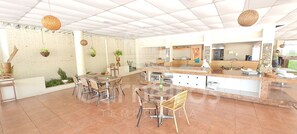 A spacious indoor area with multiple seating arrangements, a kitchen area, and hanging plants. - Flats no Beach Class de Muro Alto (Ipojuca)