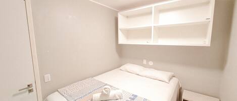 A bedroom with a bed, a bedside table, a wall-mounted shelf, and a door.