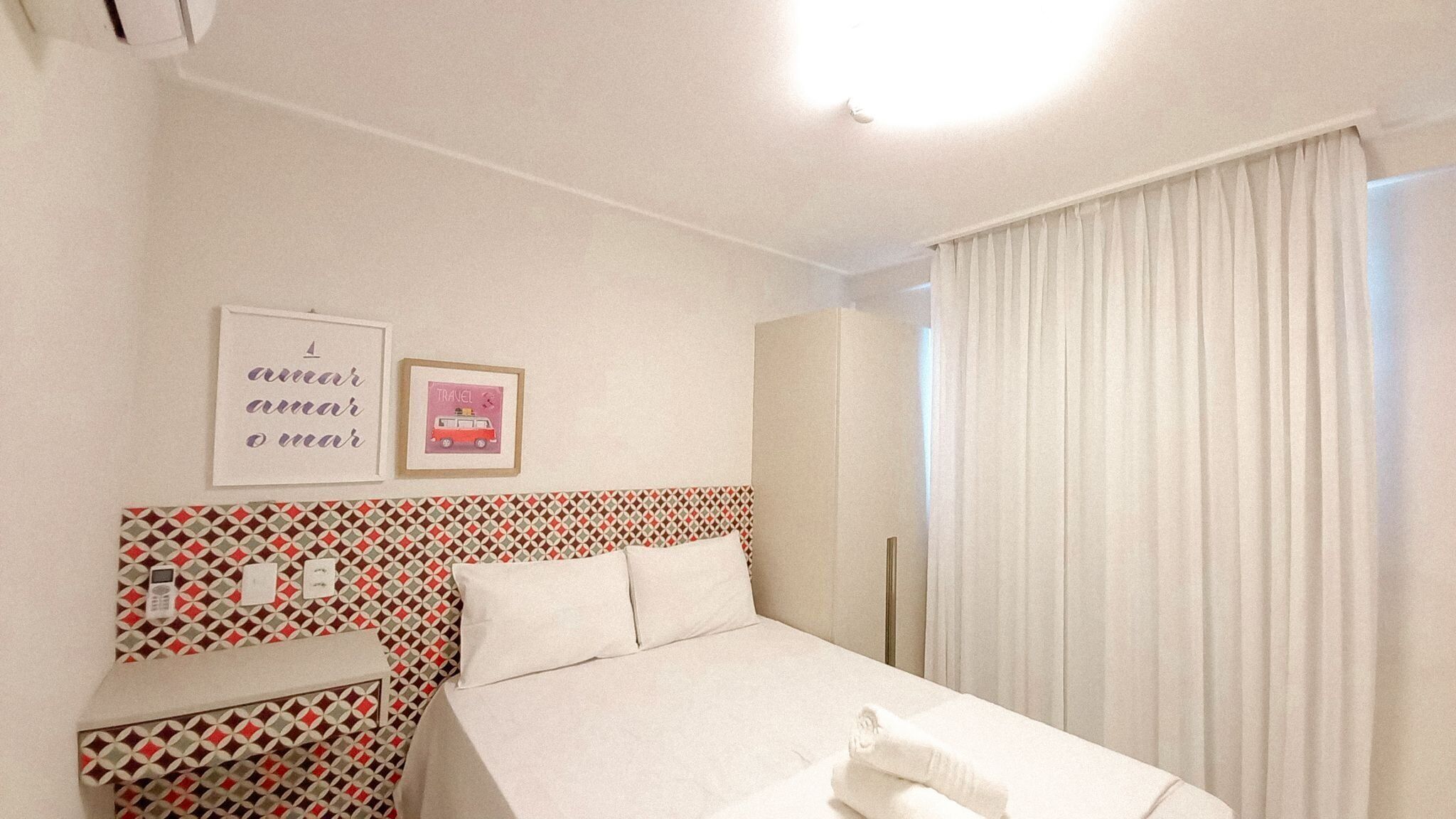 Una camera d'albergo con un letto, uno specchio, una parete con motivi geometrici e due quadri incorniciati.