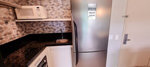A compact kitchen with a microwave, a stainless steel refrigerator, a sink, and a countertop. - Flats no Beach Class de Muro Alto (Ipojuca)