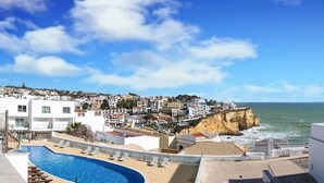 A coastal town with a cliff overlooking the sea, a swimming pool, and white buildings with red-tiled roofs. - Bay D Townhouse With Roof Top Jacuzzi and Sea Views (Carvoeiro)