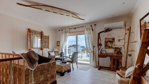A living room with a woven sofa, a dining table, and a wooden desk. - Bay D Townhouse With Roof Top Jacuzzi and Sea Views (Carvoeiro)