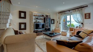 A spacious living room with a large flat-screen TV, comfortable seating, a staircase, and a view of the outdoors. - Bay D Townhouse With Roof Top Jacuzzi and Sea Views (Carvoeiro)