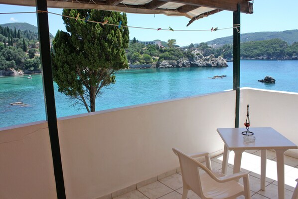 A balcony with a table and chairs overlooking a body of water with trees and hills in the background.