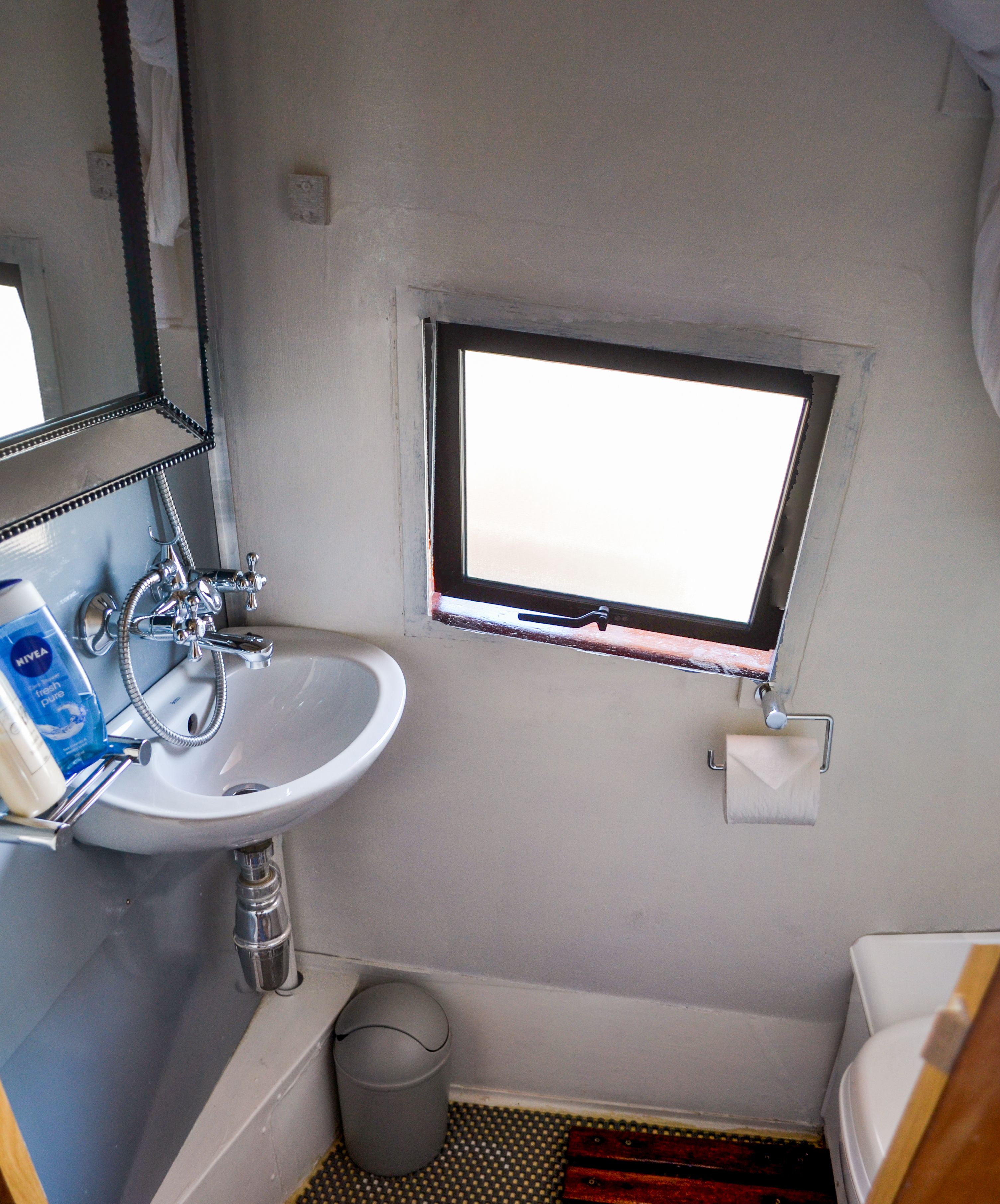 A compact bathroom with a white sink, a window, and a small mirror.