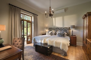 Un dormitorio con una cama grande, dos mesitas de noche con lámparas, un aparador, un banco de madera y una ventana con cortinas.