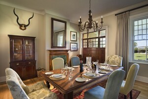 Comedor con mesa de madera dispuesta para seis comensales, sillas tapizadas, candelabro y un espejo grande sobre la chimenea.
