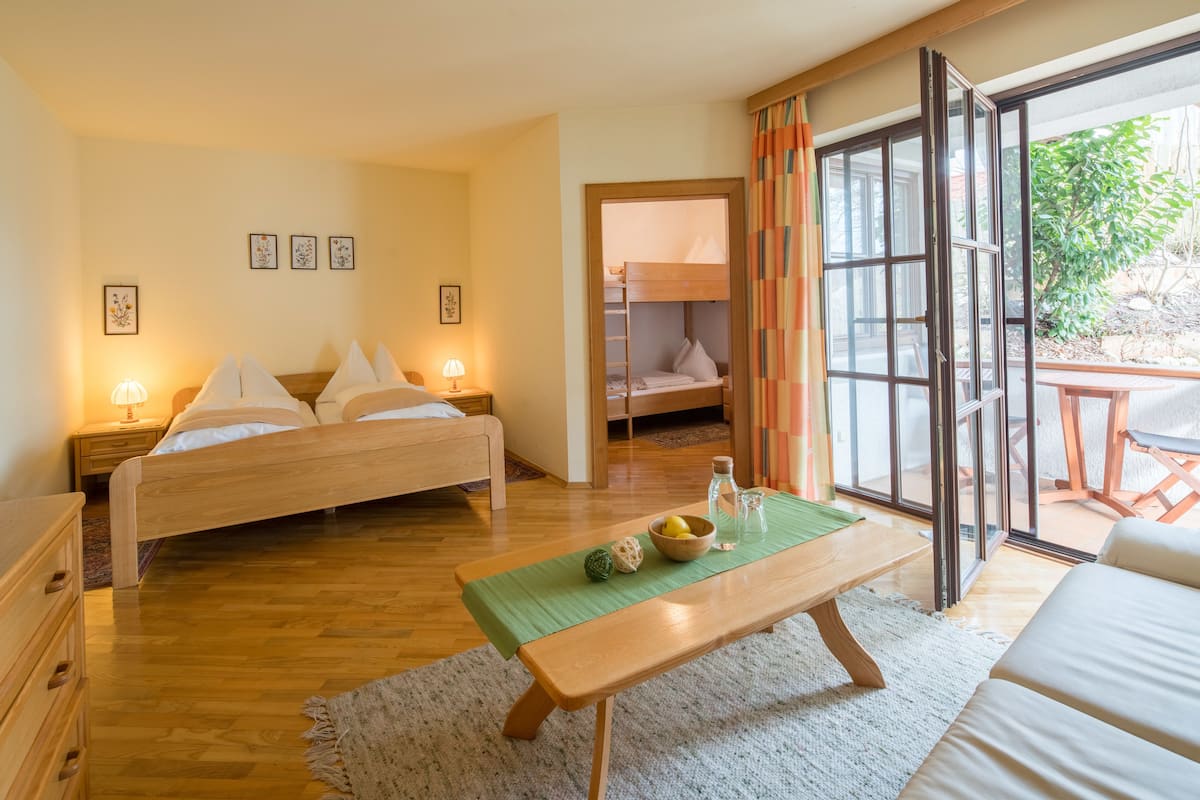 Ein Schlafzimmer mit einem hölzernen Bett, Nachttischen, einer grünen Matte und Blick durch eine Glastür.